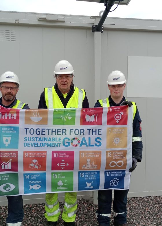 3 team members holding up the SDG flag at shieldhall WWTW